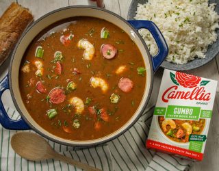 Stovetop Cajun Gumbo in a blue dutch oven featuring shrimp and sasuage next to a box of camellia brand gumbo roux base and a plate of white rice
