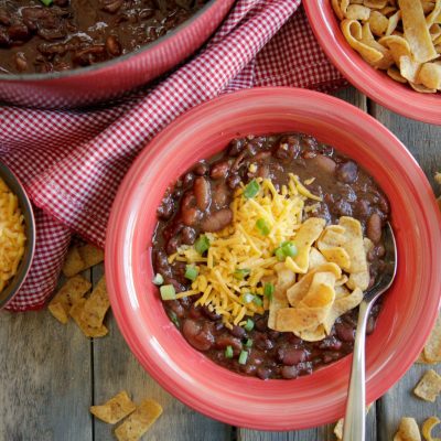 a bowl of 3 bean vegetarian chili next to frito chips, shredded cheese and a dutch oven of beans