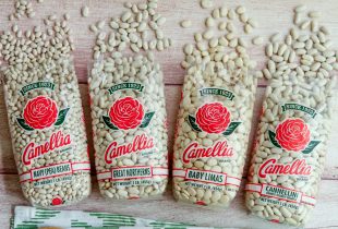 Navy (pea beans), great northerns, baby limas, ans cannellini white beans in a line on a table with the bags opened