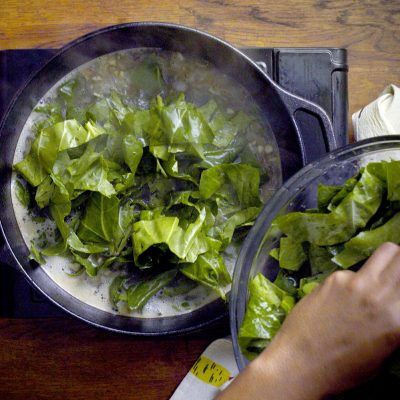 a chef adding collard greens to his pot that is cooking