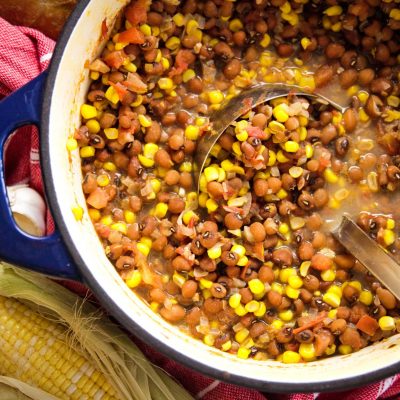 a dutch oven full of stewed tomatoes and corn peas