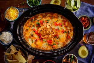 a slow cooker full of cheesy refried bean dip surrounded by various toppings