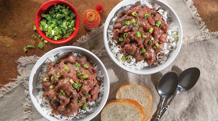 2 bowls of Red Beans and rice topped with green onions next to 2 pieces of whole white bread and a cup of chopped green onions