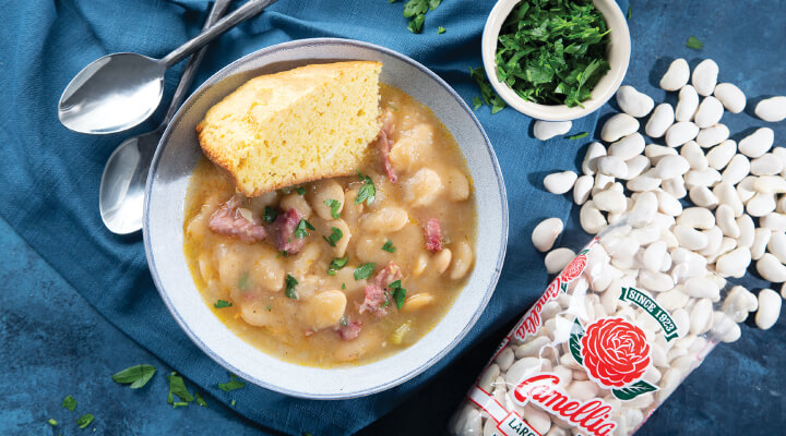 a bowl of Southern Large Limas and sausage with a side of corn bread on top next to a package of camellia brand large lima beans