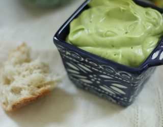 a close up of a dipping cup of avocado dressing and dip with a piece of bread