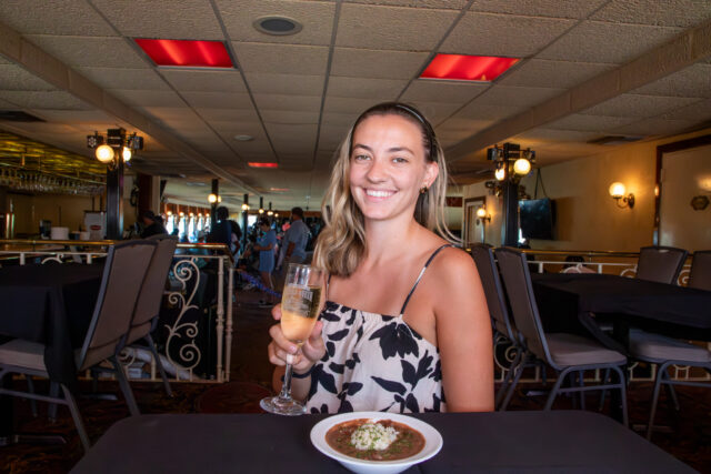 a young woman in a white sun dress drinking a glass of champagne with her red beans and rice from creole queen