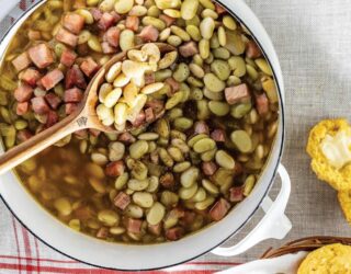 overhead image of large, white, stovetop pot on white table with white and red cloth napkin underneath and cooked butter beans inside pot